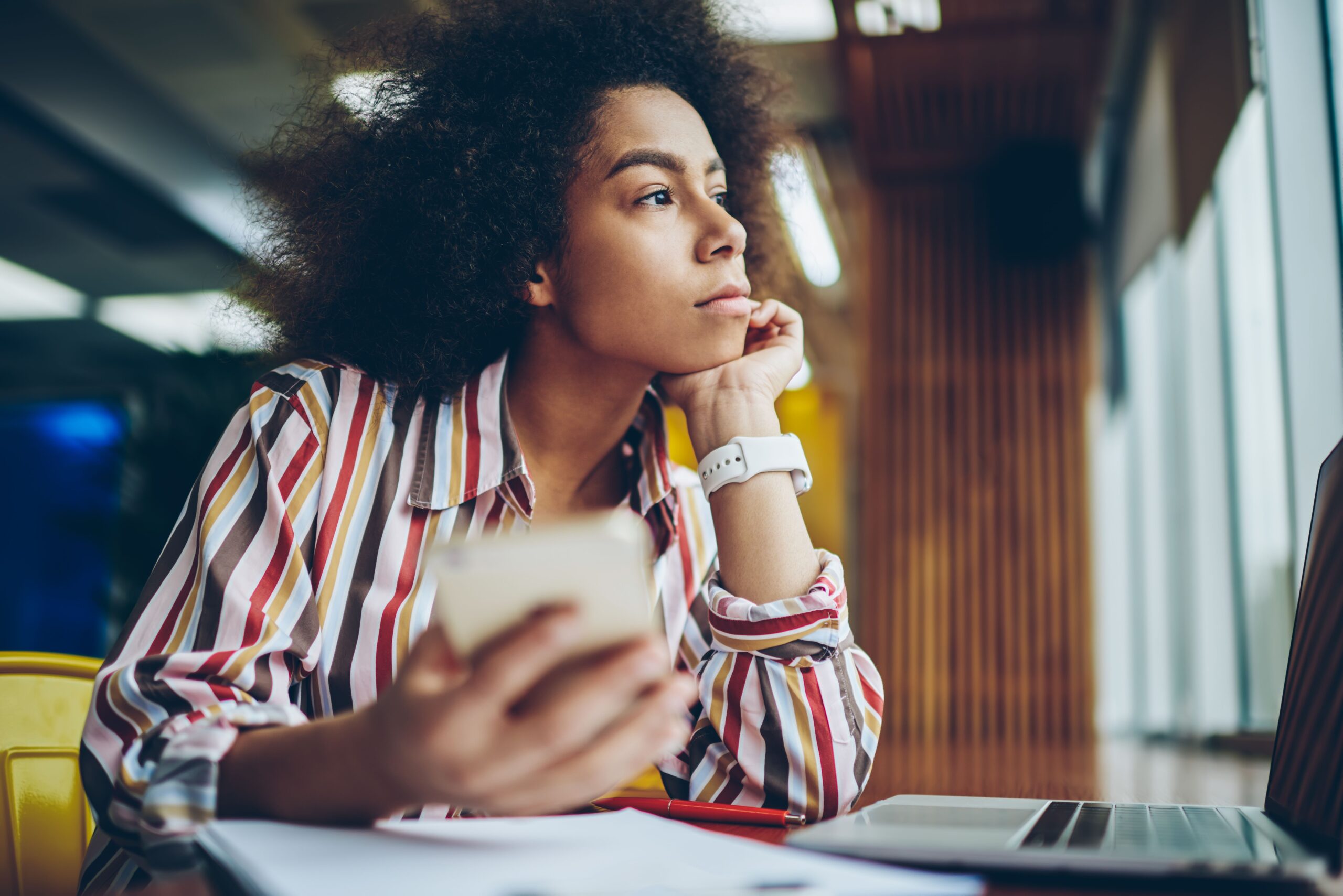 Black woman looking up from her phone and computer