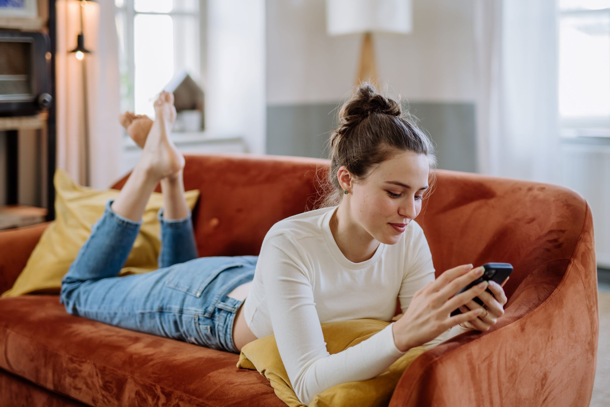 Young woman laying on her couch scrolling on her mobile phone.